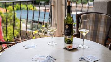 A table with a bottle of wine and two glasses on a balcony overlooking a pool.