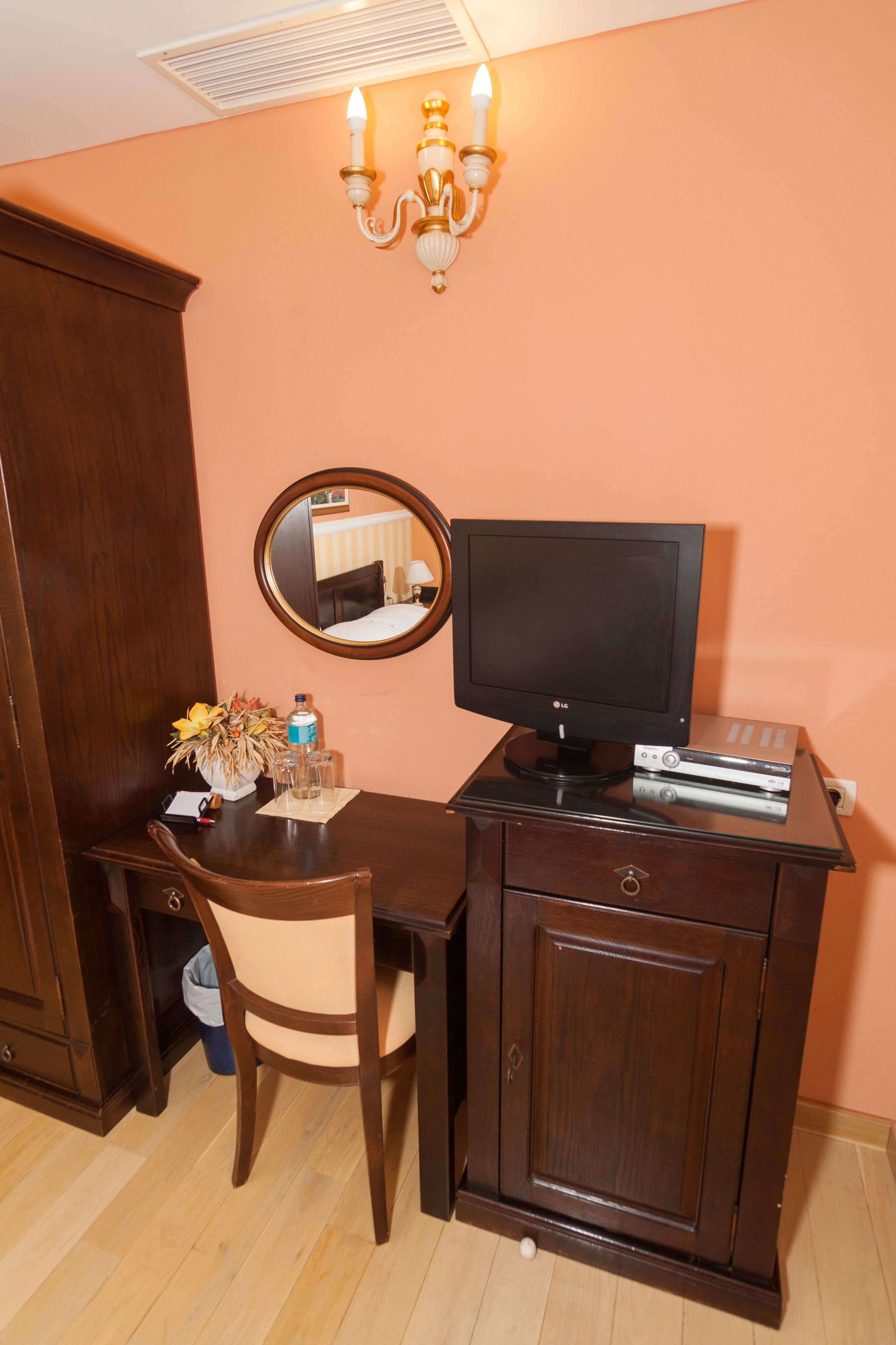 Habitación de hotel con escritorio de madera, televisor, espejo y candelabro.
