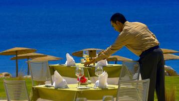 A table set for a meal with a waiter attending to it, overlooking a scenic ocean view.
