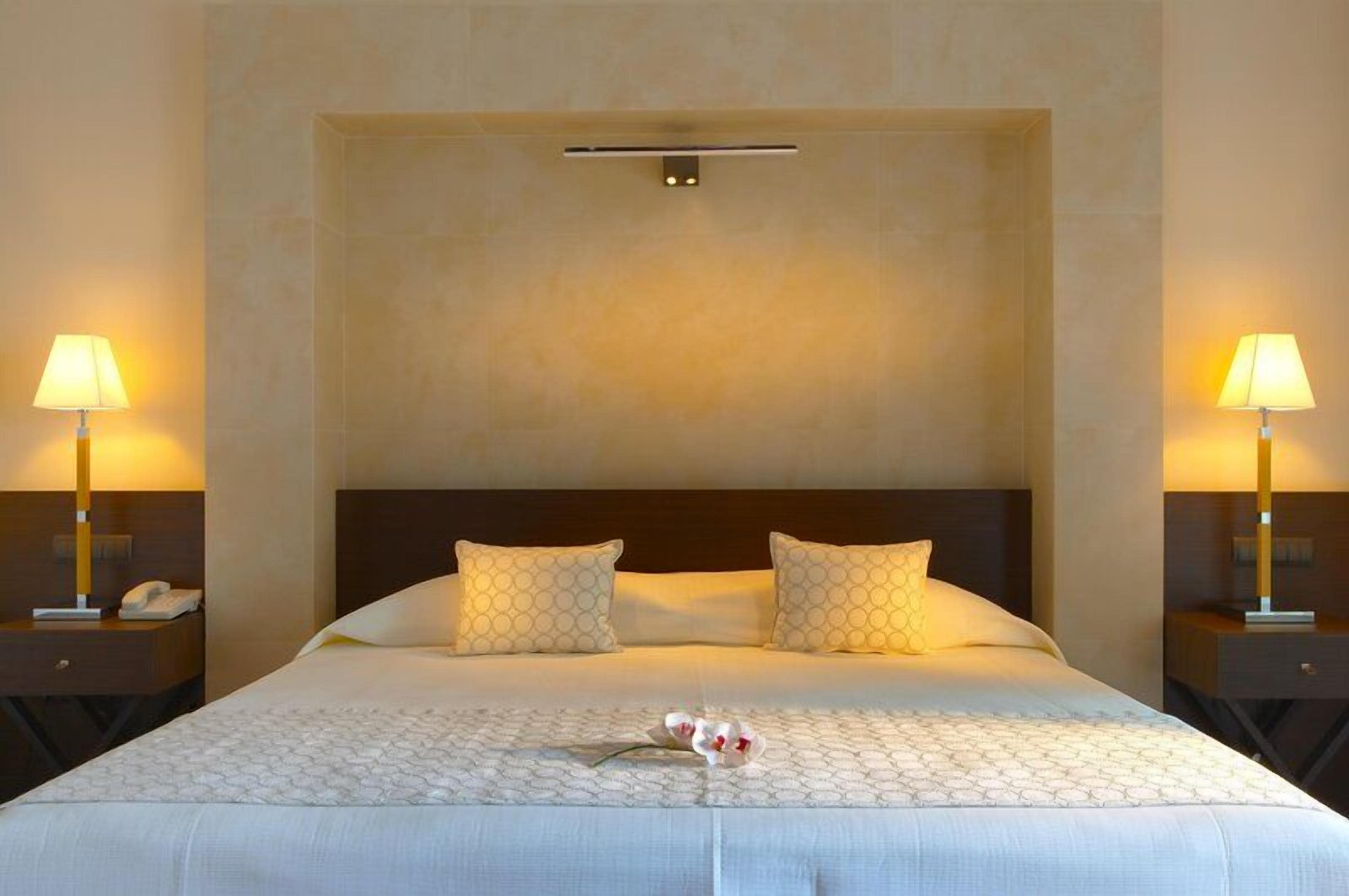 A hotel room with a large bed, two bedside lamps, and a nightstand with a phone.