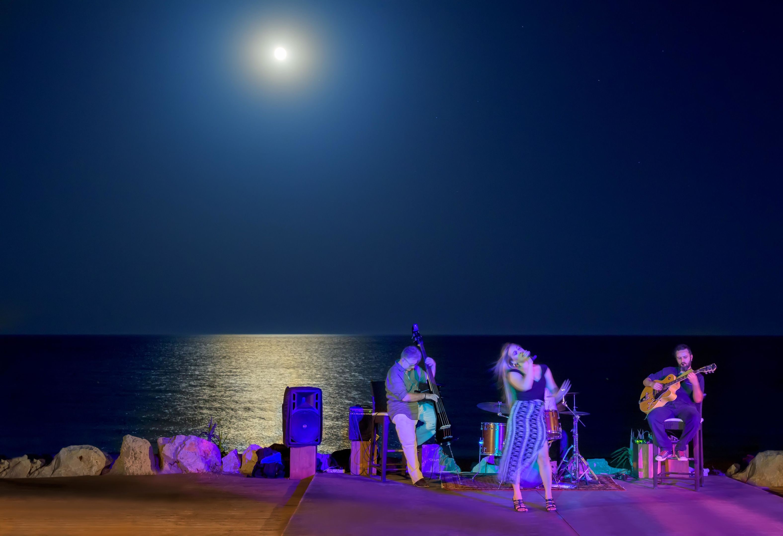 Un escenario con músicos actuando de noche frente al mar.