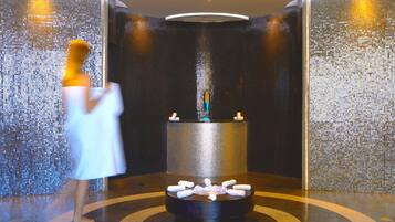 A spa area with a circular hot tub surrounded by candles, a tiled wall, and a person in a robe.