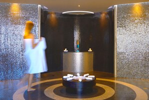 A spa area with a circular hot tub surrounded by candles, a tiled wall, and a person in a robe.