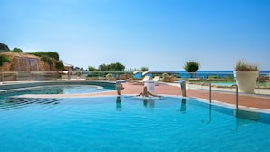A swimming pool with a view of the sea, lounge chairs, and a waterfall feature. - Elysium Resort & Spa (Rhodes)