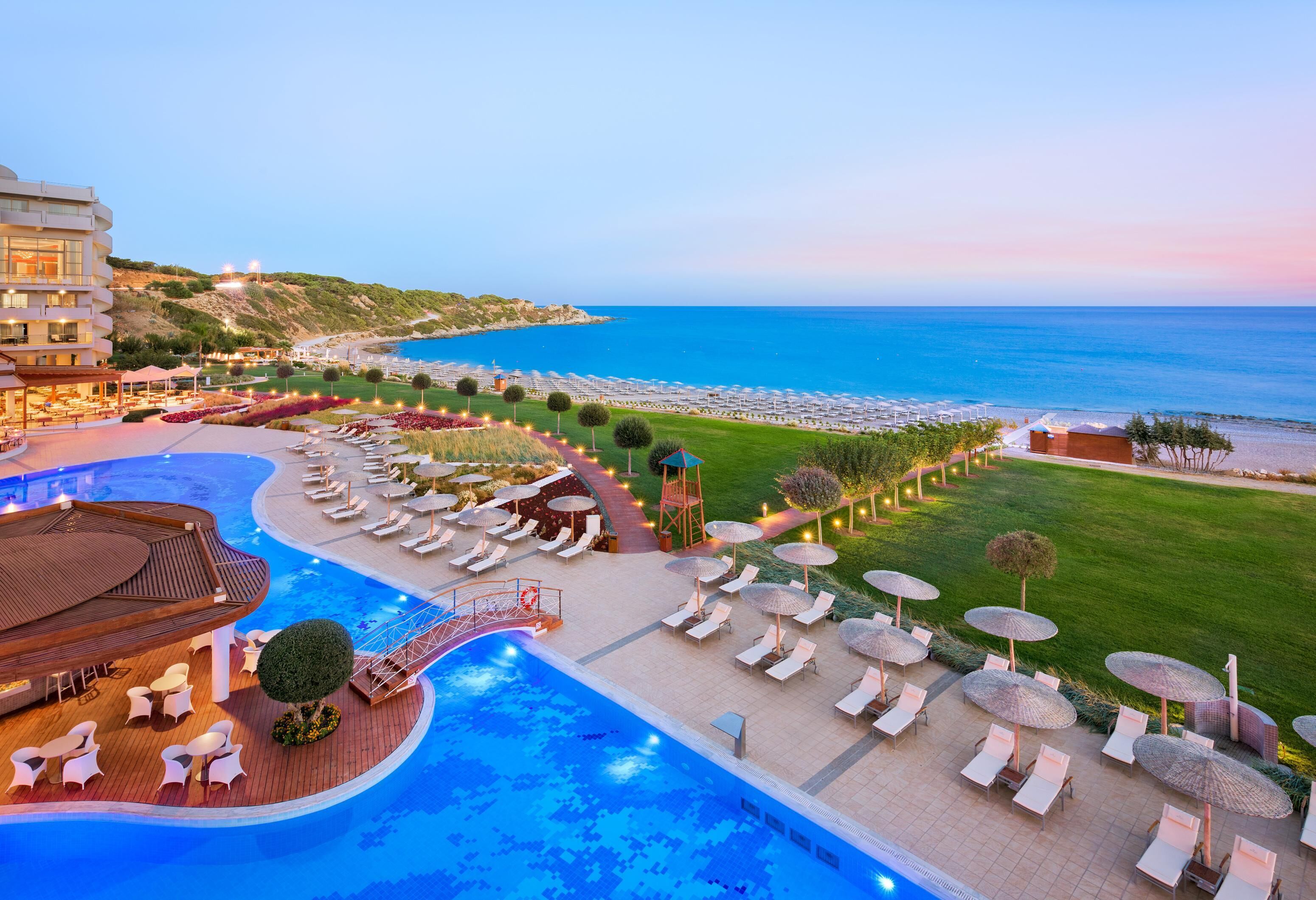 A resort with a swimming pool, lounge chairs, umbrellas, and a view of the sea.