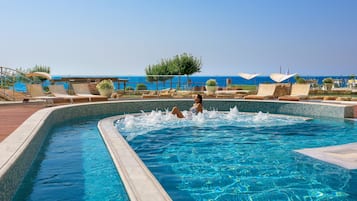 A swimming pool with lounge chairs and a view of the sea.