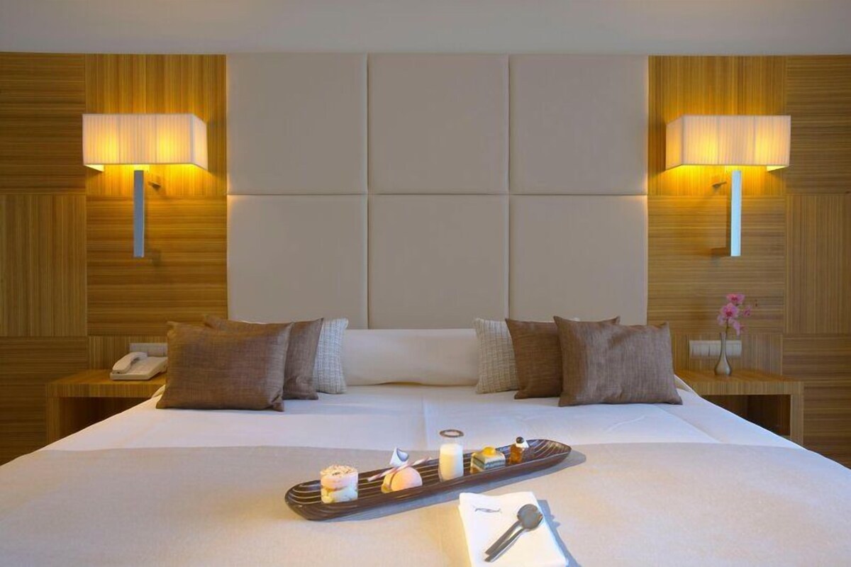 Habitación de hotel con una cama grande, dos lámparas de noche, una mesita de noche con un teléfono y una bandeja con comida y una llave.
