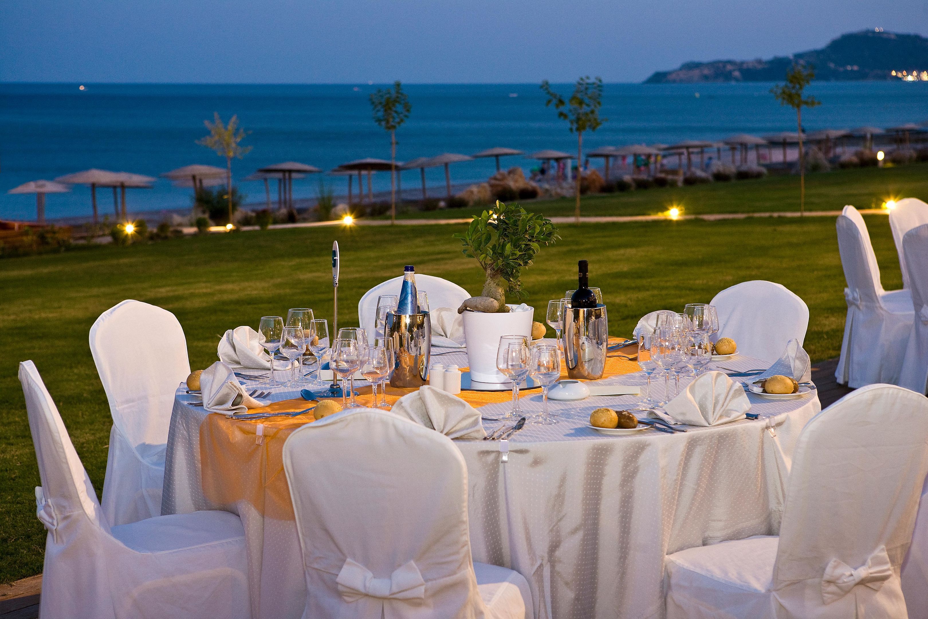Un espace de restauration en plein air, avec des tables dressées pour un repas, donnant sur une zone côtière agrémentée de parasols et offrant une vue sur la mer.