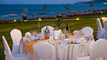 Un espace de restauration en plein air, avec des tables dressées pour un repas, donnant sur une zone côtière agrémentée de parasols et offrant une vue sur la mer.