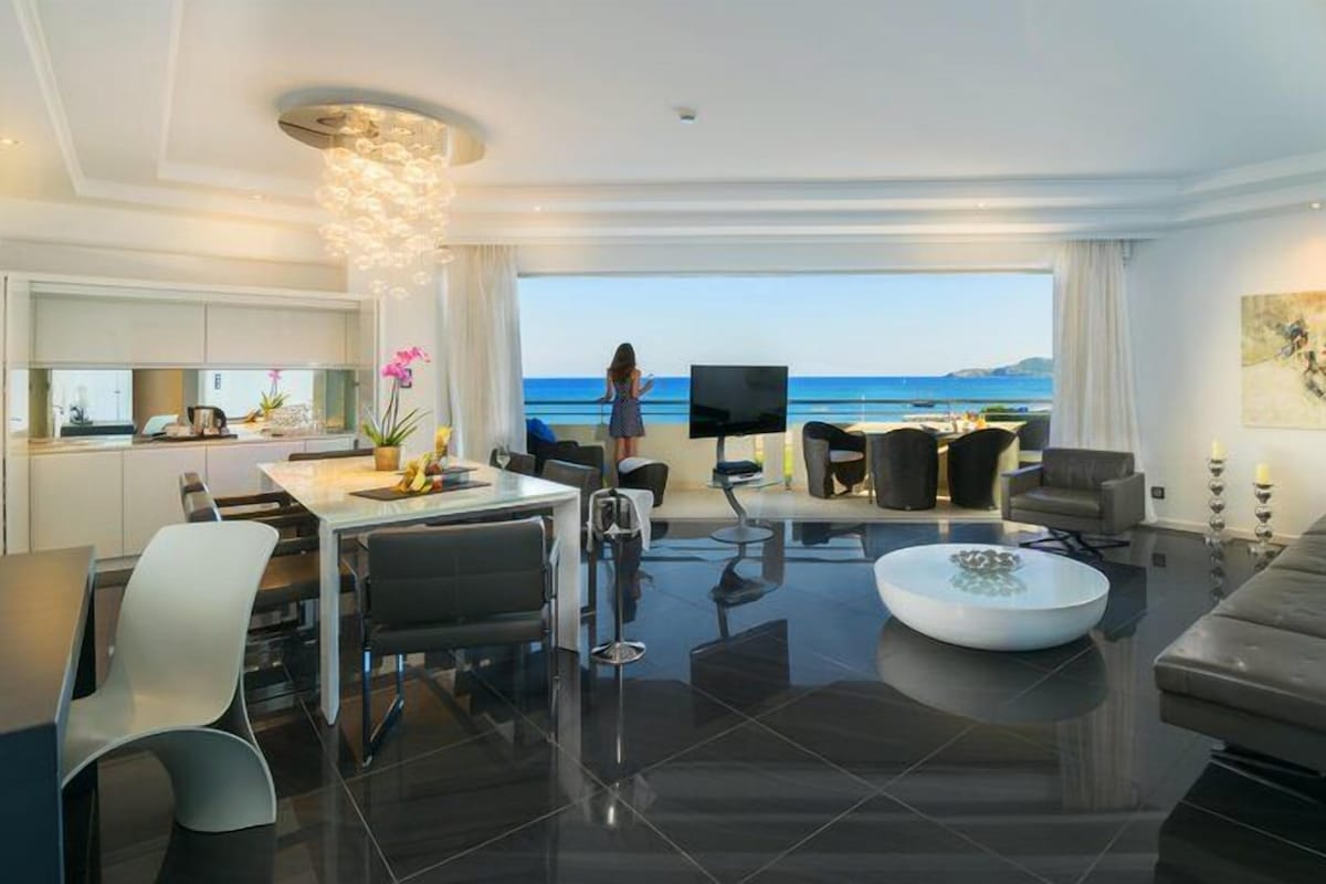 Un salón moderno con comedor, un televisor grande y vista al mar.