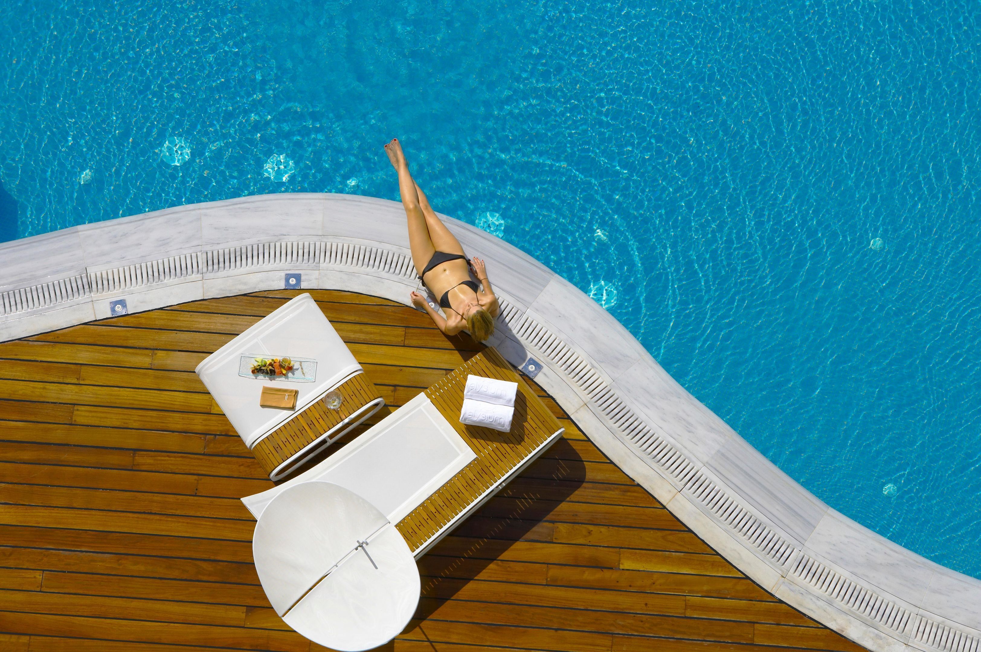 A poolside area with a wooden deck, lounge chairs, and a table with a sunshade.