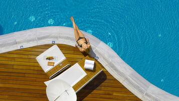 A poolside area with a wooden deck, lounge chairs, and a table with a sunshade.