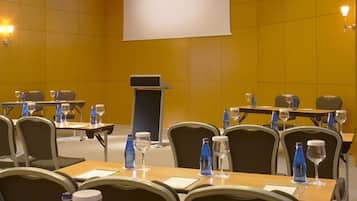 Un salón de conferencias con mesas, sillas, botellas de agua y vasos.