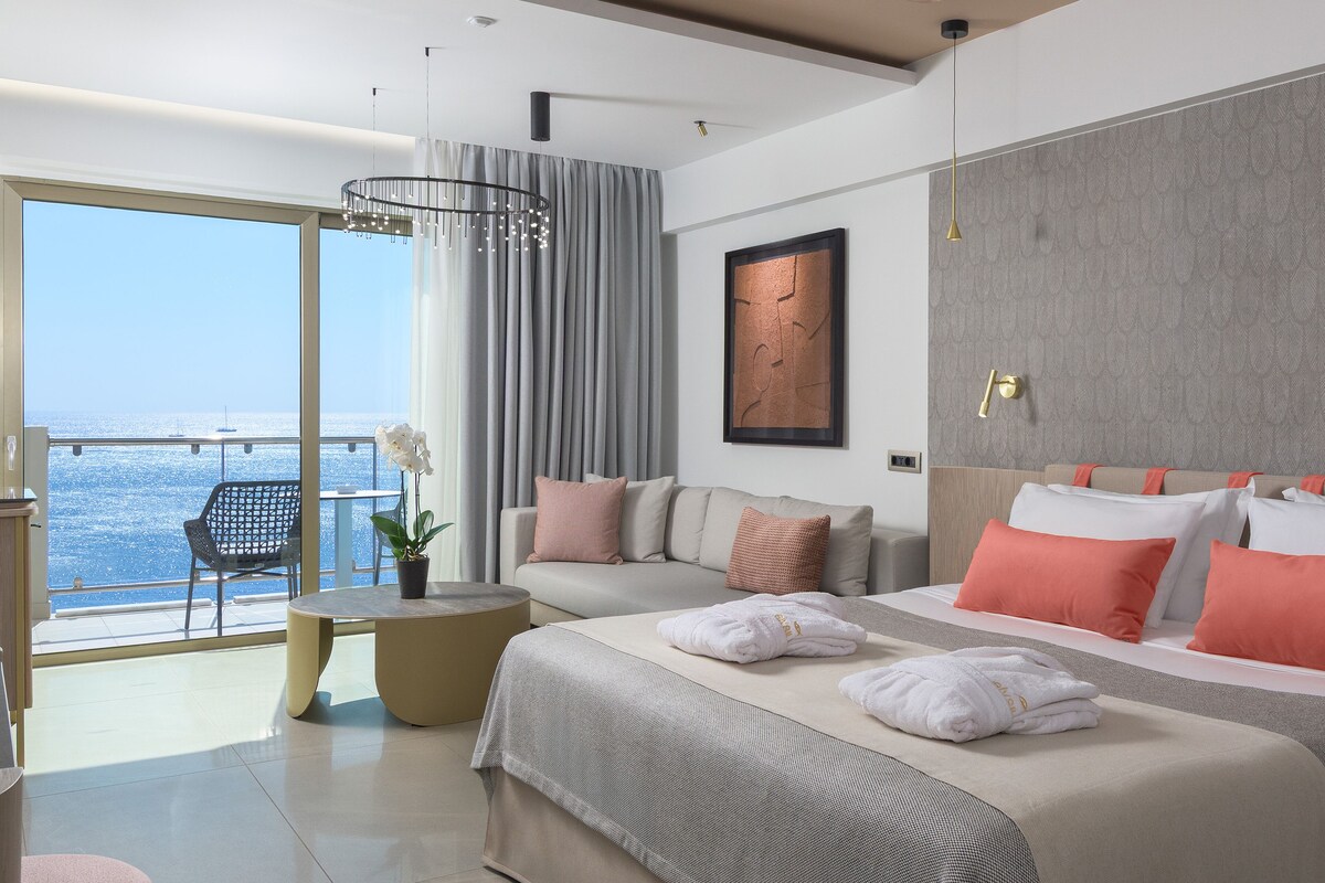 Una habitación de hotel moderna con una cama grande, un área de descanso con vista al mar y una mesa de comedor.