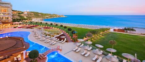 A resort with a swimming pool, lounge chairs, umbrellas, and a view of the sea.