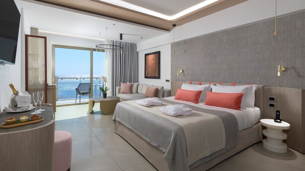A modern hotel room with a large bed, a sitting area with a view, and a balcony.