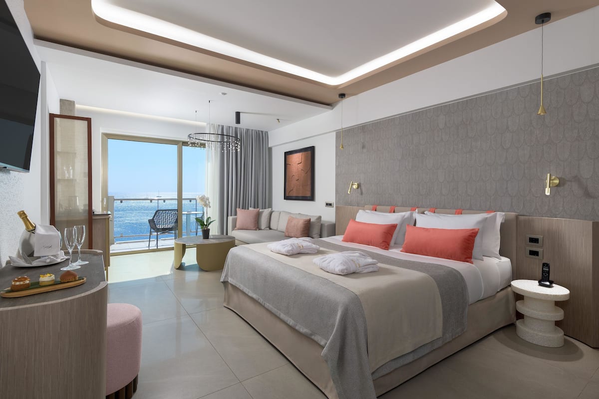 A modern hotel room with a large bed, a sitting area with a view, and a balcony.