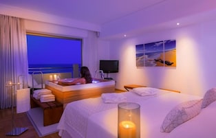 Habitación de hotel con una cama grande, bañera, televisión y ventana con vista al mar.