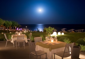 Un área de comedor al aire libre con mesas dispuestas para dos, sillas y un centro de mesa con velas.