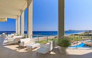 A balcony with white wicker furniture, a potted plant, and a view of the beach and ocean. - Elysium Resort & Spa (Rhodes)