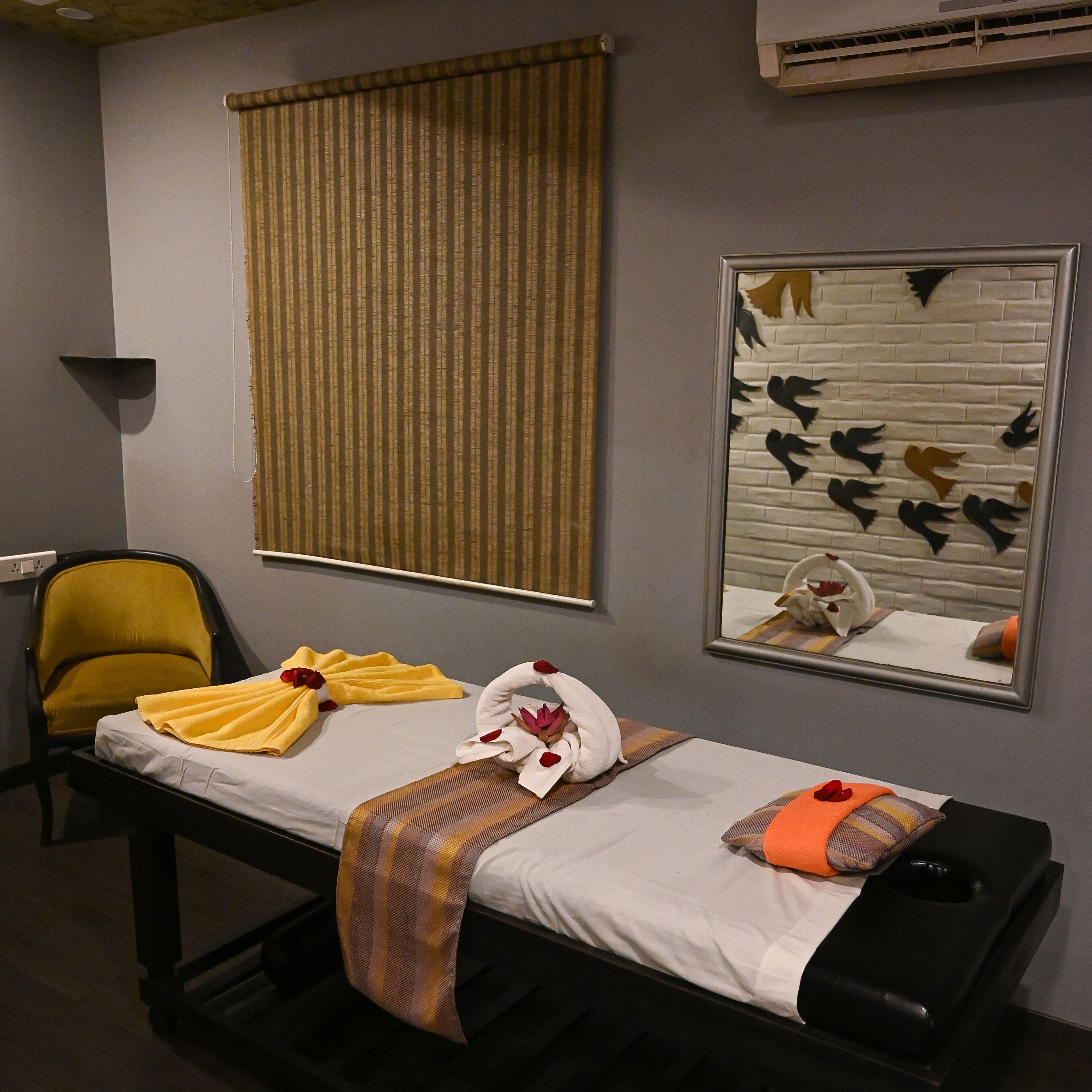 Une chambre d’hôtel comprenant un lit, une chaise, une fenêtre avec des stores, un miroir fixé au mur et une décoration murale représentant des oiseaux.