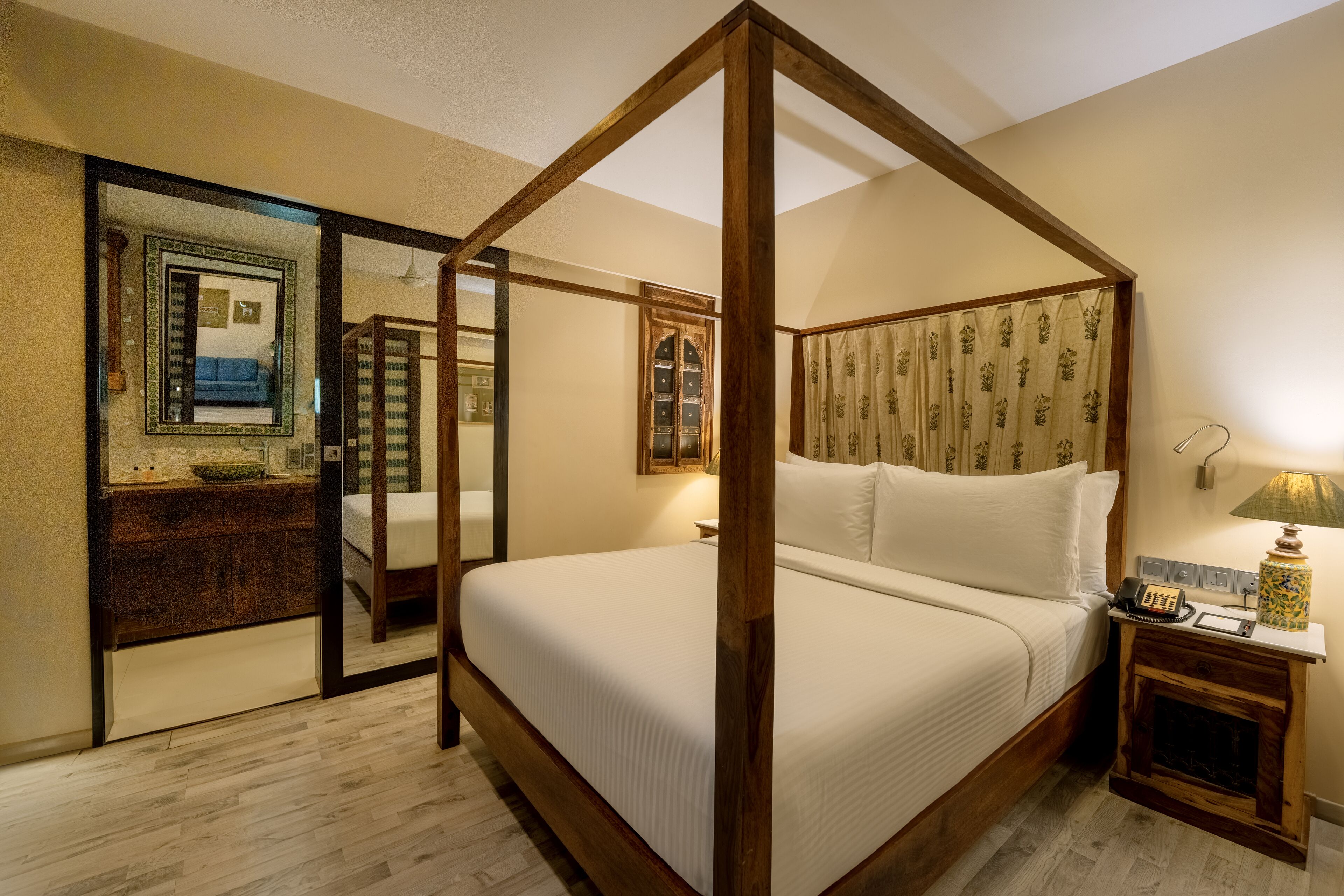 A four-poster bed with a wooden frame, a bedside table with a lamp, and a mirror on the wall.
