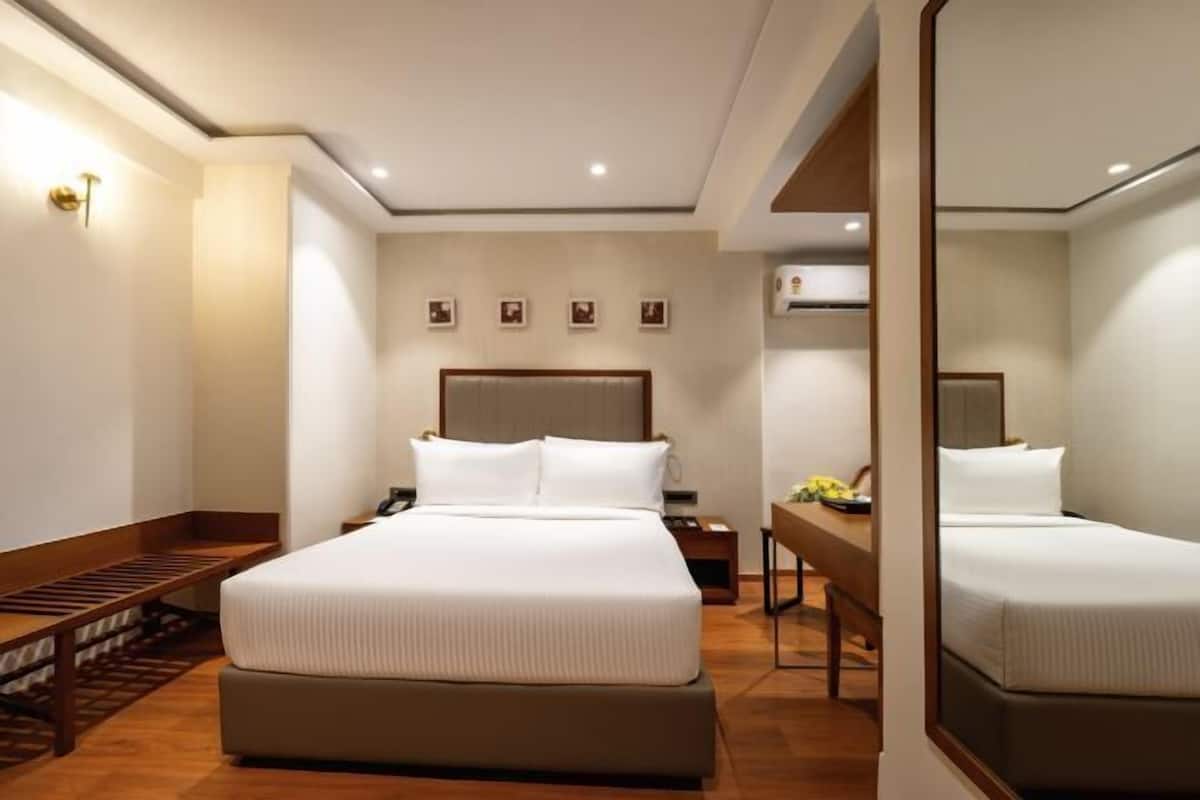 A hotel room with a large bed, bedside tables, a desk, and a mirror.
