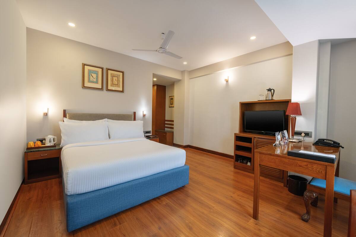 A hotel room with a bed, a desk, a television, and a ceiling fan.