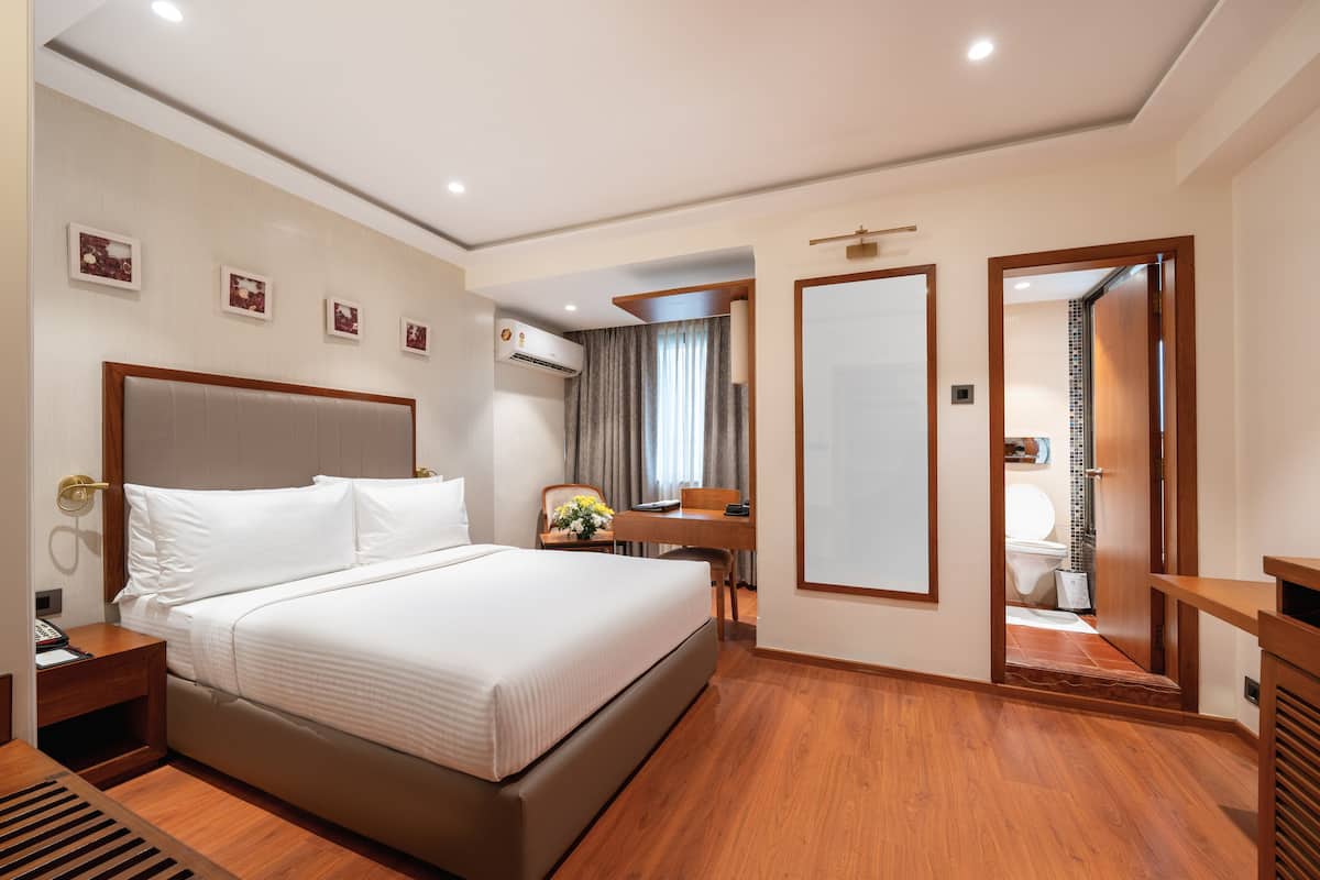 A hotel room with a large bed, bedside table, and a desk with a chair. There is a bathroom visible through an open door.