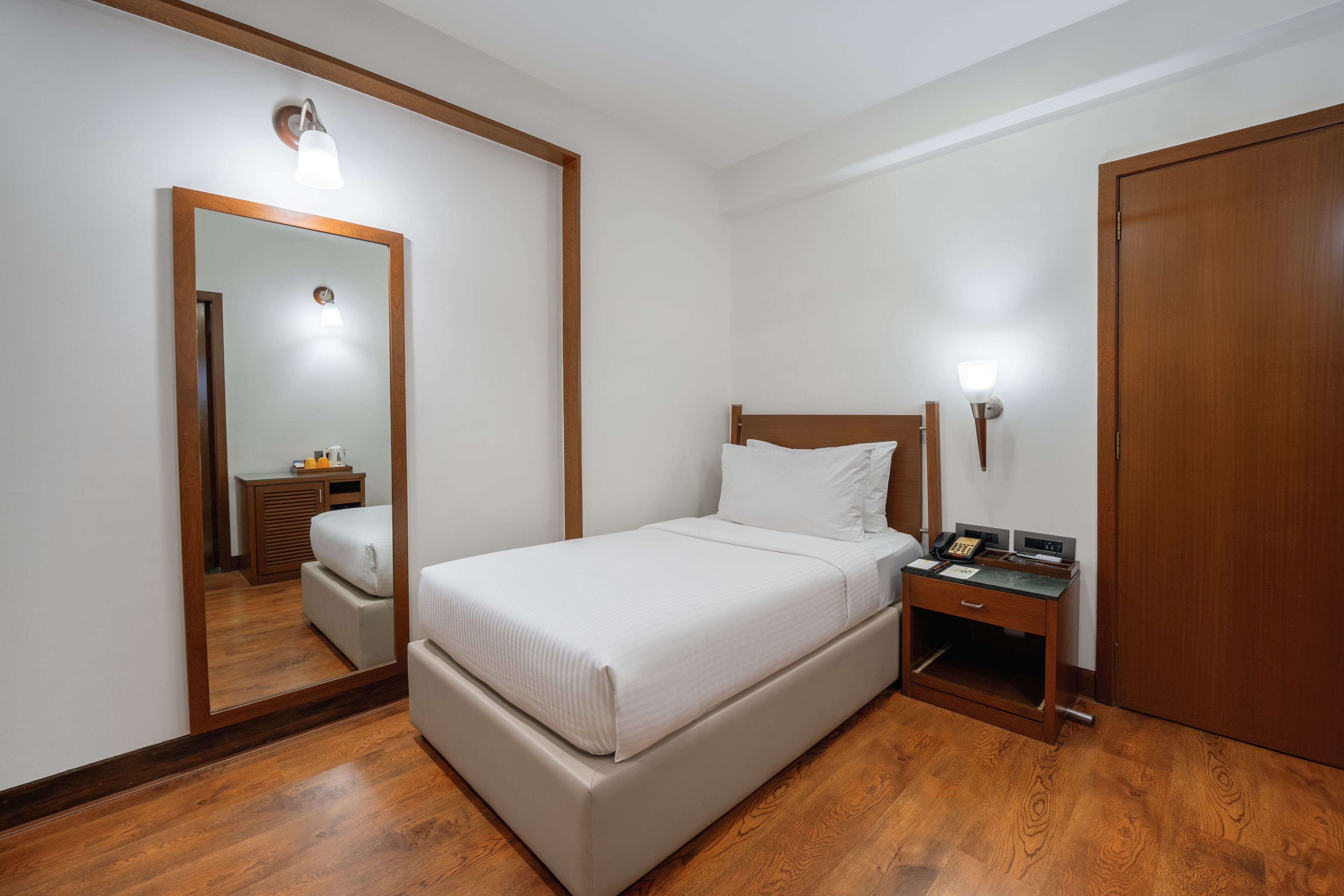 A bedroom with a bed, bedside table, nightstand, and a wooden wardrobe.