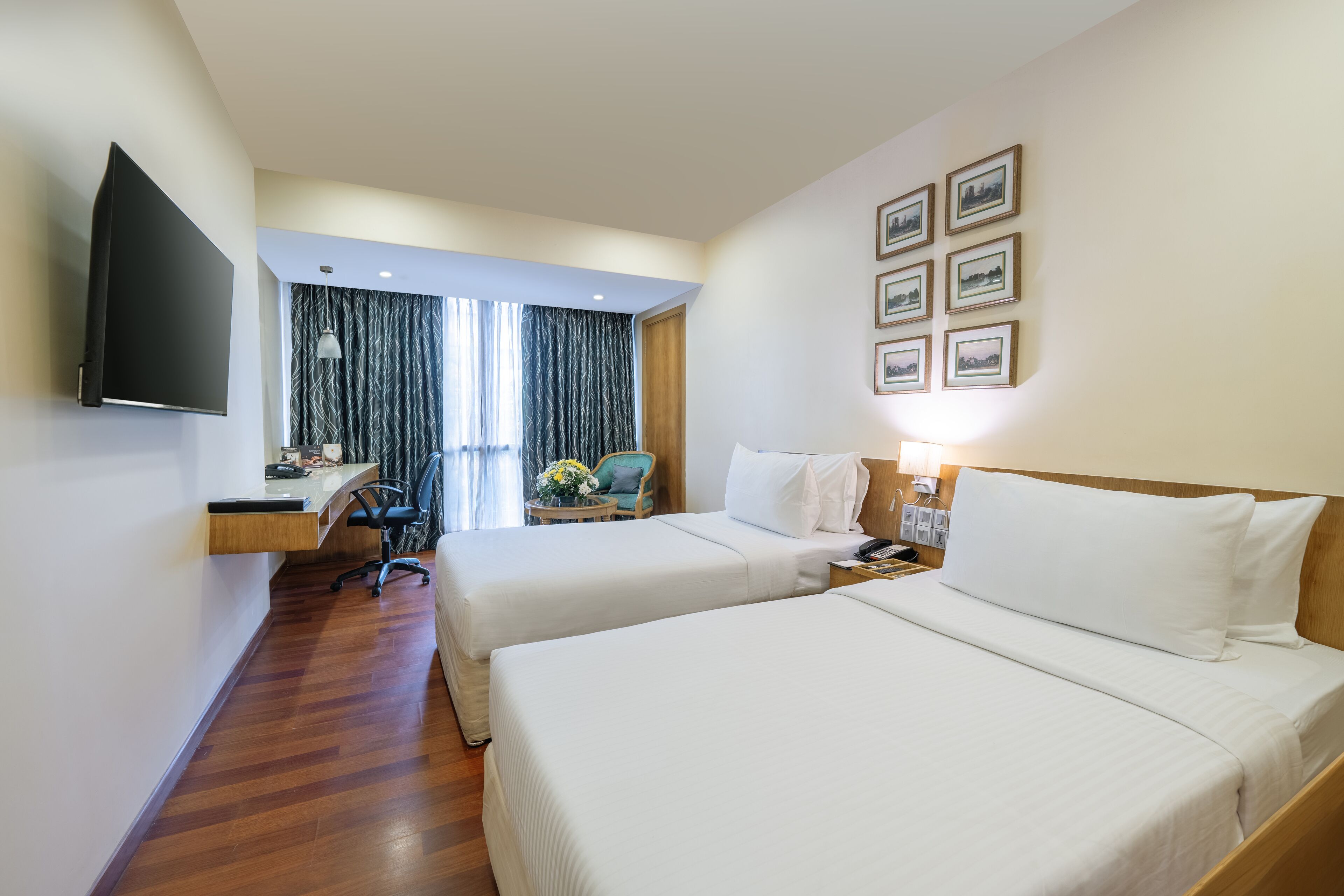 Una camera d'albergo con due letti, una scrivania, una sedia, una TV e una finestra con tende.