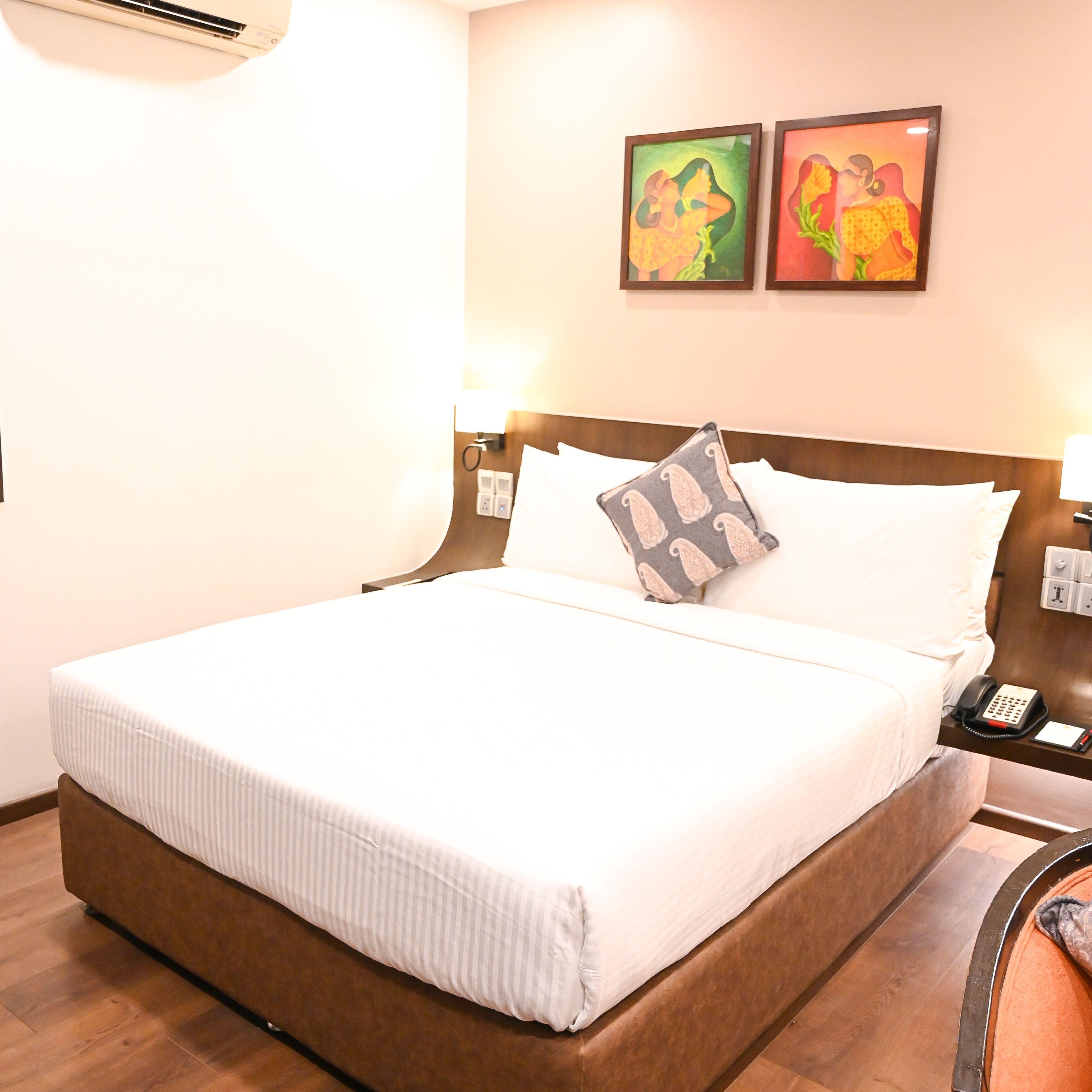 A neatly made bed with a striped bedspread, a pillow with a paisley pattern, and a bedside table with a telephone and a lamp.