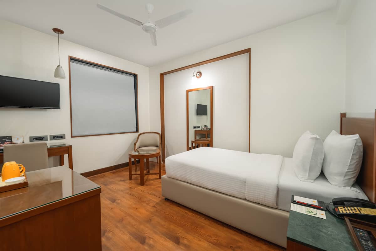 A hotel room with a bed, desk, chair, and a flat-screen TV.