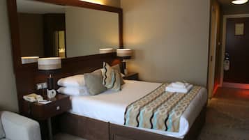 Habitación de hotel con una cama grande, una mesita de noche con lámpara, un espejo y una silla.