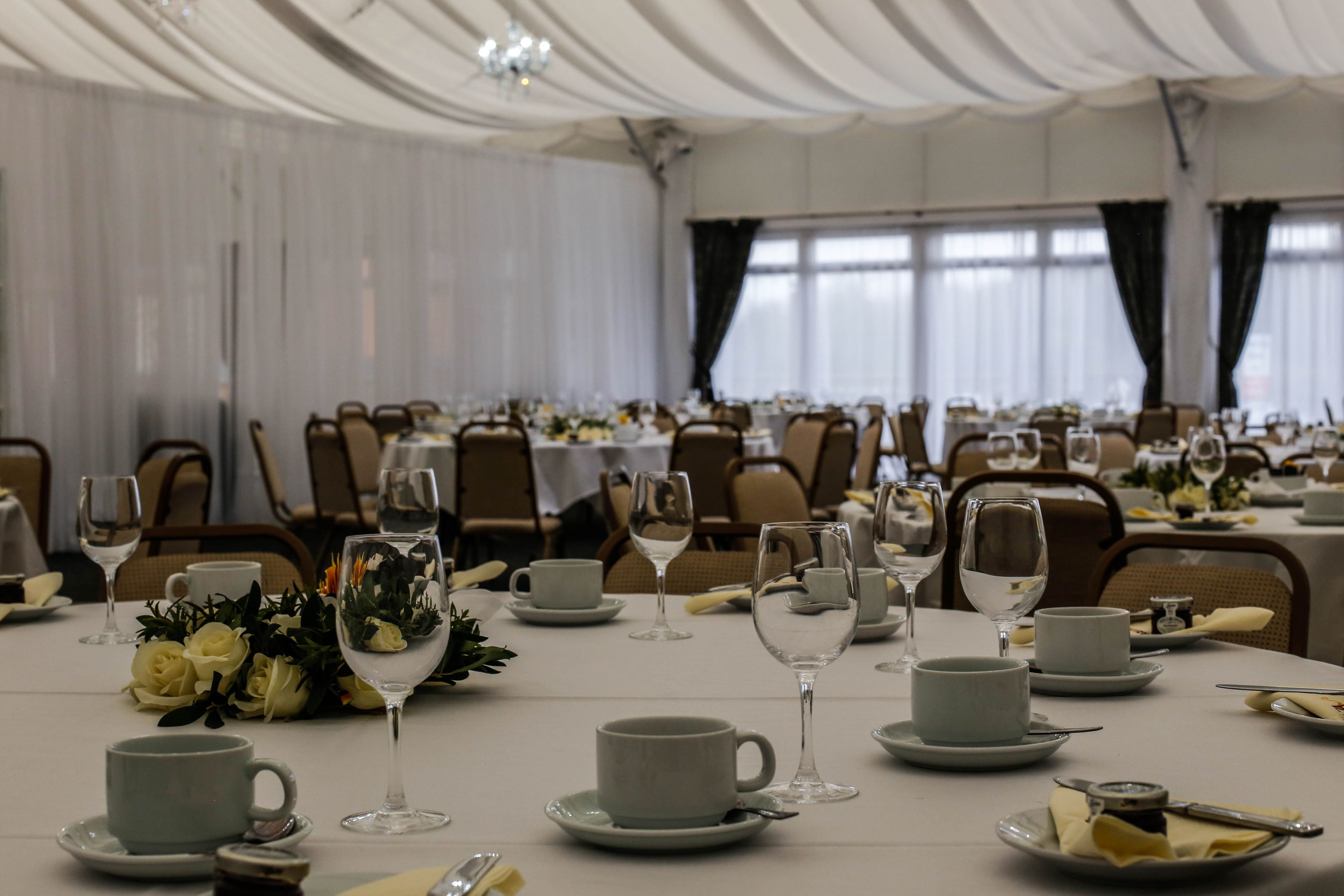 Un salón de banquetes con mesas dispuestas para un evento formal, que incluye manteles blancos, centros de mesa florales y cubertería ordenada.