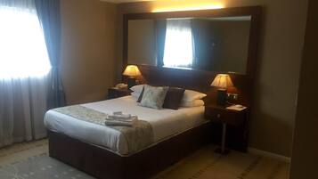 Ein Hotelzimmer mit einem großen Bett, zwei Nachttischen mit Lampen, einem großen Spiegel über dem Bett und einem Fenster mit Vorhängen.