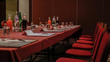 A conference room with a long table, red chairs, and various bottles and glasses on the table.