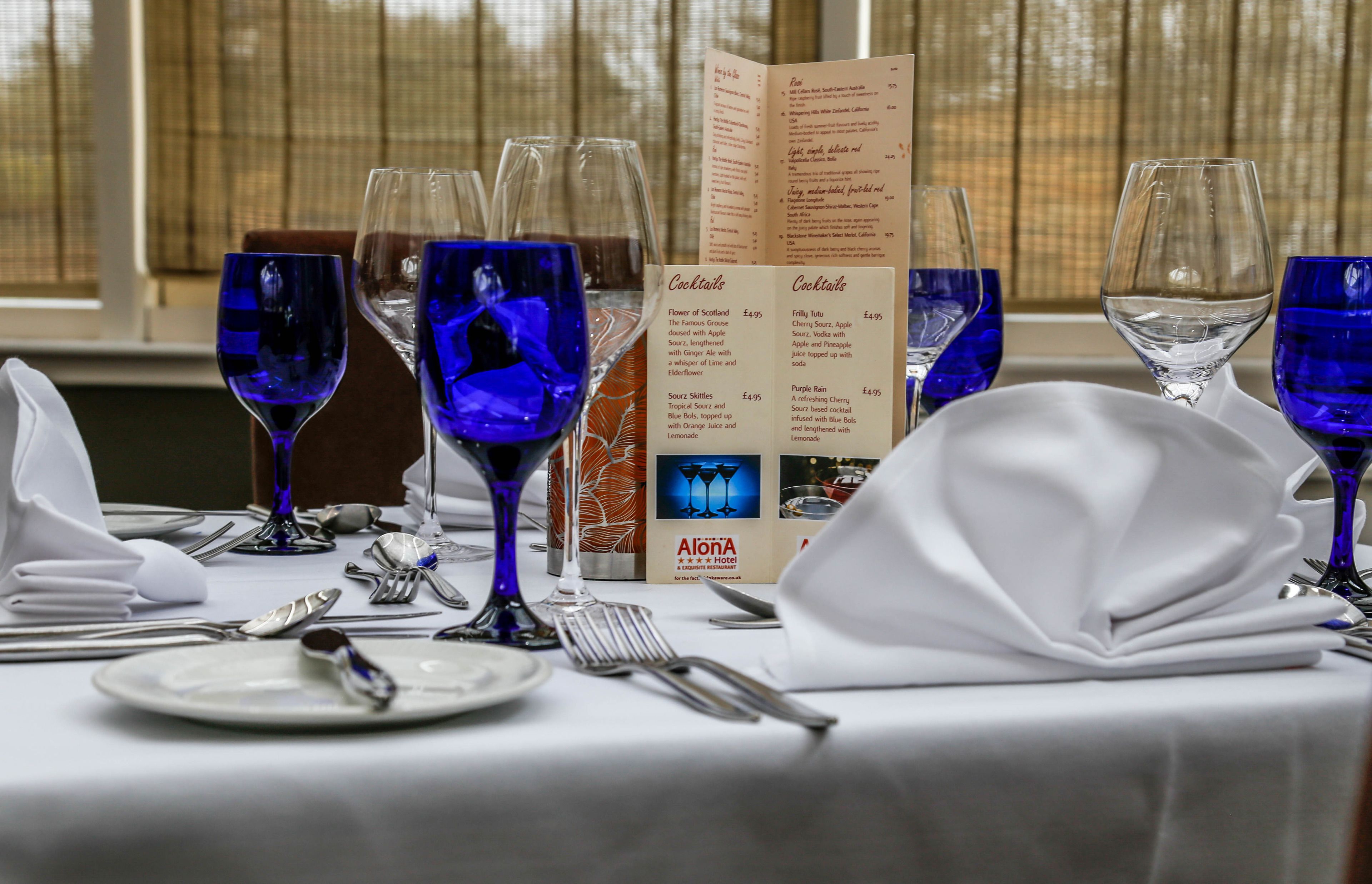 A table set for dining with a menu and a bottle of Alona Hotel wine.