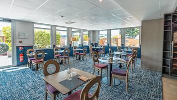 Un comedor de hotel con varias mesas y sillas, ventanas amplias y una alfombra azul.