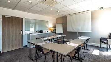Une salle de conférence équipée d’un écran de projection, d’un tableau blanc et d’un coin cuisine.