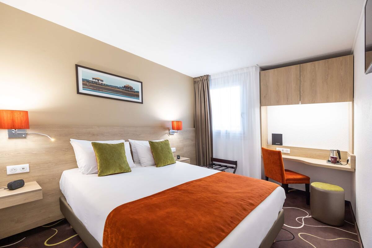 A hotel room with a bed, a desk, a chair, and a window with curtains.