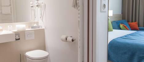 Habitación de hotel con baño, una cama con almohadas de colores, un inodoro blanco y un espejo.