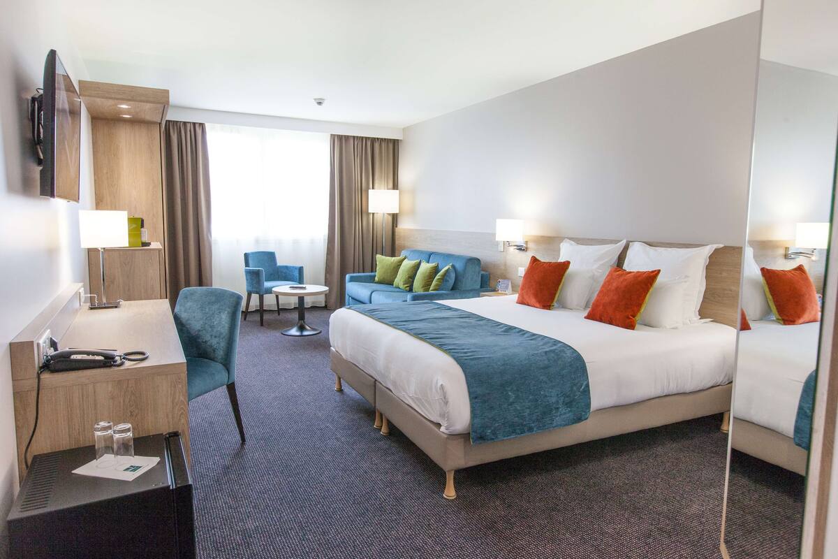 A hotel room with a large bed, a desk, a chair, and a small table.