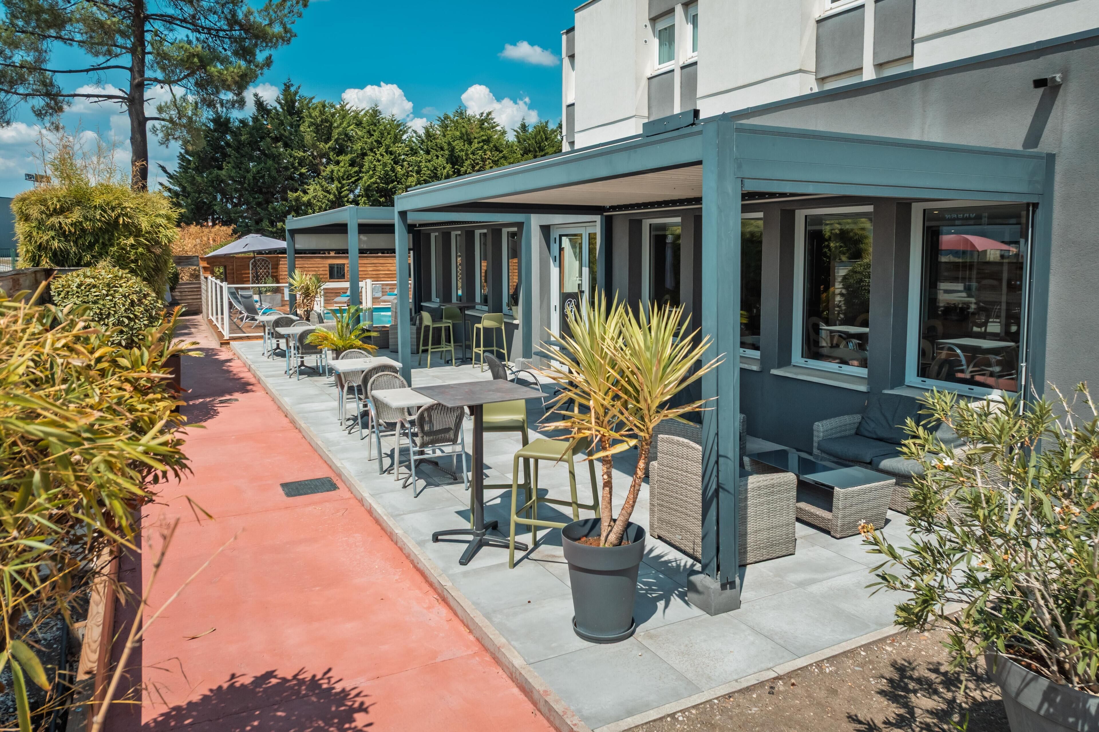 A covered outdoor seating area with tables and chairs, a pool, and a building with large windows.