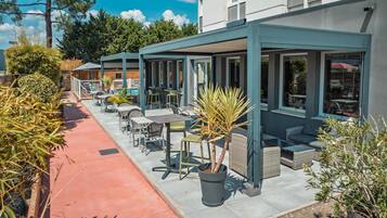 A covered outdoor seating area with tables and chairs, a pool, and a building with large windows.
