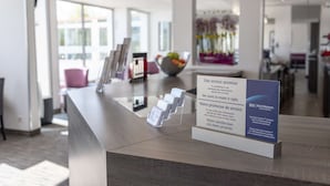 Un mostrador de recepción con un cartel en inglés y francés, un interior moderno con un separador de vidrio y vistas al exterior a través de grandes ventanales.