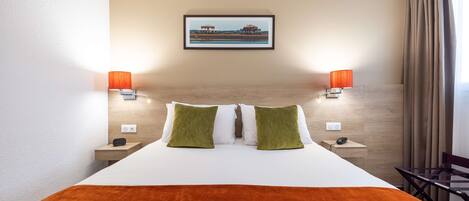 A hotel room with a large bed, two bedside lamps, a framed picture on the wall, and a view of the outdoors.