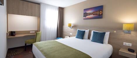 Une chambre d’hôtel comprenant un lit, un bureau, une chaise, une table de chevet et une lampe fixée au mur.