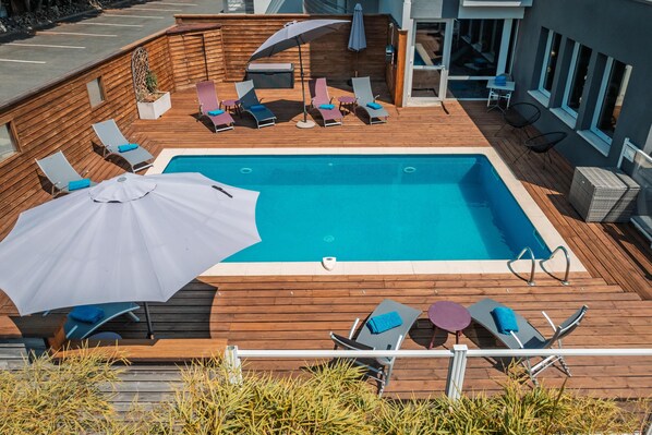 Piscina rodeada de un deck de madera, sillas de descanso y sombrillas.