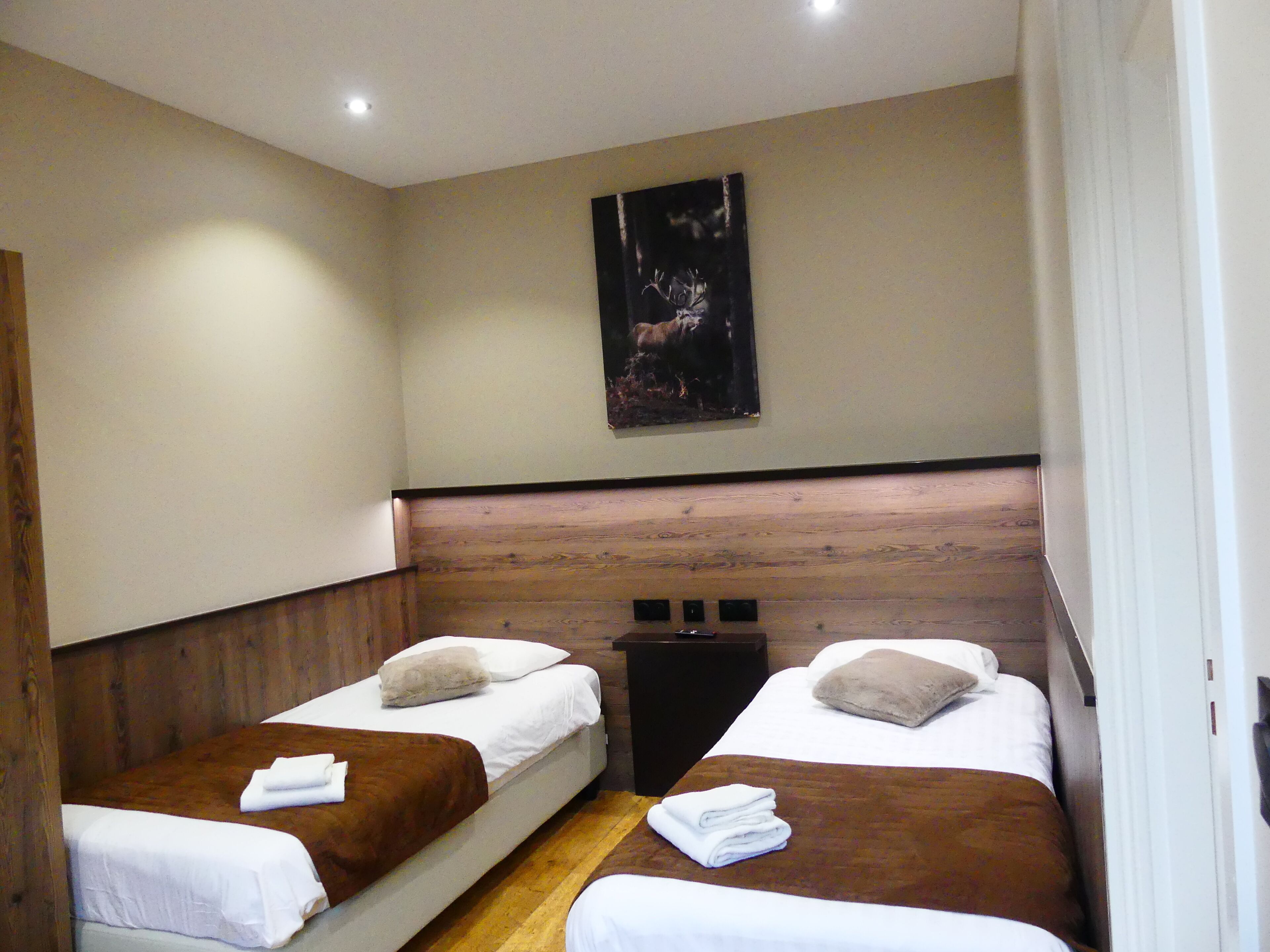 A hotel room with two single beds, wooden headboard, a mounted painting, and a wooden floor.